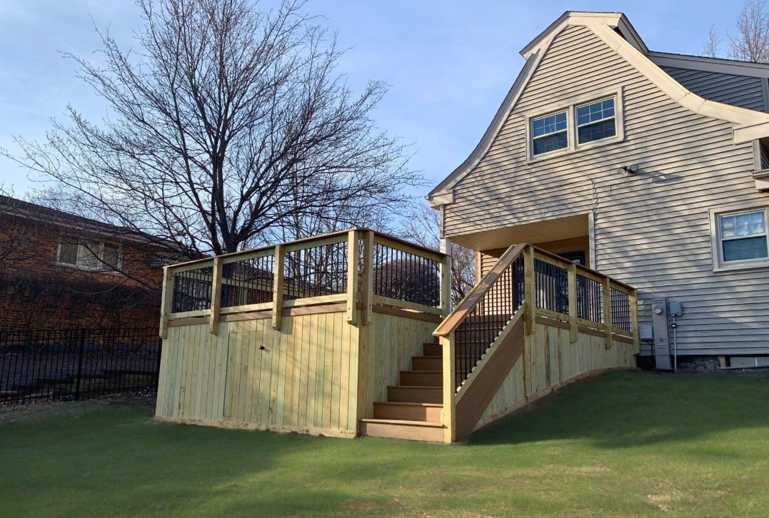 Large, newly constructed wooden deck with black metal balusters, stairs, and an enclosed lattice base, extending from a residential home in Homer Glen.